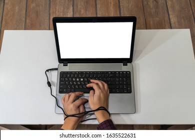 Modern Slavery Concept. Above View Of A Man Hands Typing On A Laptop And Tied With The Charging Cable.