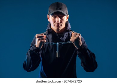 Modern Slavery. Man Shows Chain Around His Neck. Young Man Demonstrates Bondage Symbols. Contemporary Inmate With Padlock Around His Neck. Guy Is Prisoner On Dark Background. Portrait Of Modern Slave