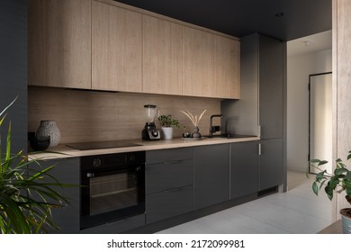 Modern and small kitchen with wooden cupboard and countertop and black furniture, oven, sink and fridge