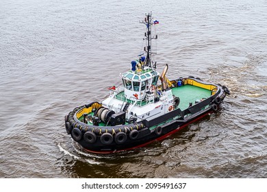 A modern small tugboat cruises in the water area of the port. Preparing to maneuver a large ship