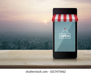 Modern smart mobile phone with on line shopping store graphic and open sign on wooden table over city tower at sunset, vintage style, Shop online concept - Shutterstock ID 1017475462