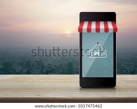 Modern smart mobile phone with on line shopping store graphic and open sign on wooden table over city tower at sunset, vintage style, Shop online concept