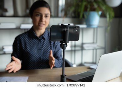 Modern smartphone gadget on tripod record young female speaker or coach making live broadcast on Internet, cellphone gadget shoot woman blogger or influencer talking for tutorial or webinar online