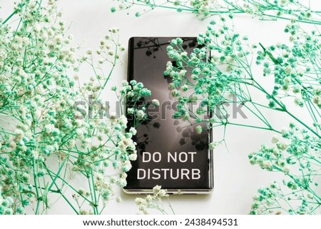 Modern smartphone - a mobile phone with the inscription do not disturb among many green dried flowers. Psychological concept of rest and seclusion of introvert with nature. Photo. Close-up