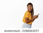 Modern smiling black girl using smartphone, turn head behind, looking at empty space, concept of cellular technology and people connection