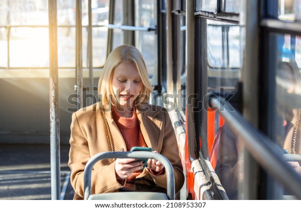 Modern smiling\
cute woman sitting in a bus . Smiling and looking away. Bus\
journey. Woman using her cell phone on bus. Tramway. Sms, message.\
Woman with phone at the public\
transport