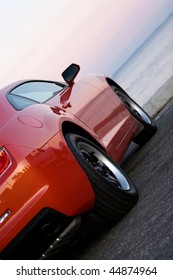 A Modern Sports Car Parked At The Beach Around Sunset.