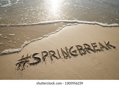 Modern Spring Break Message Handwritten With A Social Media Hashtag On The Smooth Sand Of An Empty Beach With An Oncoming Wave