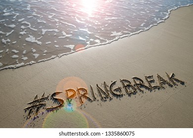 Modern Spring Break Message Handwritten With A Social Media Hashtag On The Smooth Sand Of An Empty Beach With An Oncoming Wave