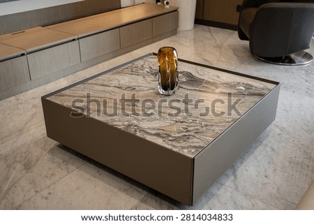 Modern square marble coffee table with amber glass vase in luxury living room.