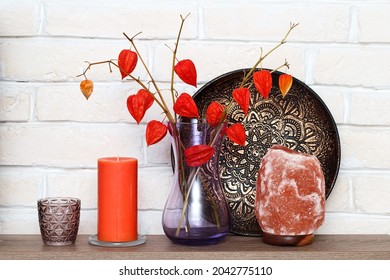 A Modern Still Life With An Aromatic Candle And A Salt Lamp. Bright Orange Decor For Home And Office. Decorative African Plate And Vase With Physalis