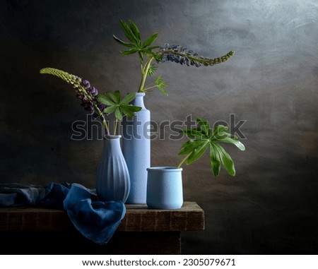 Modern still life with lupins in blue vases on a dark background.