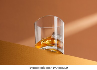modern still life in warm colors. glass with whiskey with ice on the edge of the surface in the rays of light.