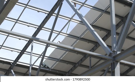 Modern storehouse construction site, structural steel structure of new commercial building against. Construction of modern factory or warehouse. Crane lowers roofing. Man working on roof
