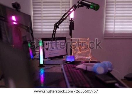 Modern streaming desk setup featuring computer monitor microphone RGB lighting headphones and subscribe sign for live stream content creation