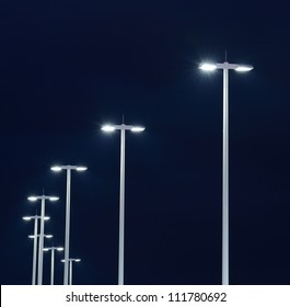 Modern Street Lights Illuminated At Night Against A Dark Sky