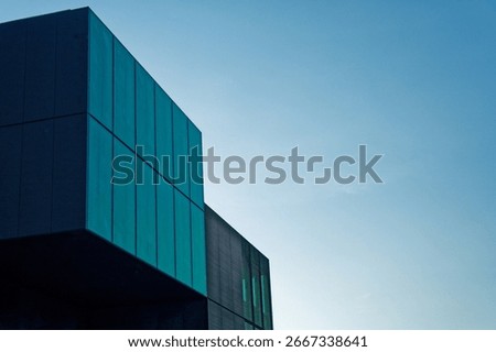 A modern structure with a dark graphite green facade and a black side extension features a windowless design of rectangular blocks creating a sleek contemporary architectural appearance