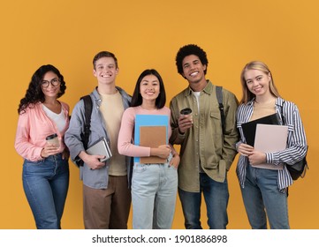Modern students from different countries and exchange program. Smiling young international people with cups of takeaway coffee, books and backpacks look at camera, isolated on orange background