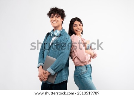 Modern Students. Happy Young Couple With Laptop And Workbooks Posing Standing Back To Back On White Studio Background, Smiling To Camera. Technology And Education, Great E-Learning Offer Concept