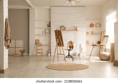 Modern studio interior with artist's workplace and foldable wooden easel near large window - Powered by Shutterstock