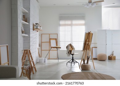 Modern studio interior with artist's workplace and foldable wooden easel near large window - Powered by Shutterstock