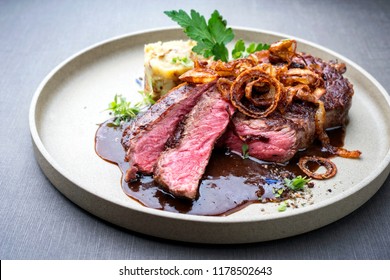 Modern style barbecue dry aged sliced roast beef with fried onion rings and mashed potatoes as closeup on a plate 
