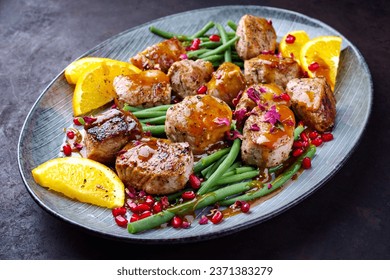 Modern style jusy seared pork pigllet tenderloin fillet meat medallions with orange relish sauce, pomegranate and green baby beans vegetable served as close-up on