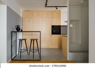 Modern Style Kitchen With Birch Plywood Cupboards, Black Table With Tall Bar Stools And Concrete Wall And Ceiling