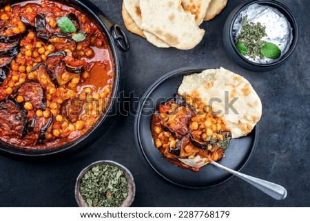 Modern style slow cooked Lebanese vegetarian eggplant stew maghmour served with chickpeas and pita bread as top view in a design pot 
