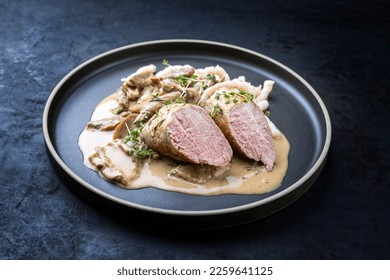 Modern style traditional barbecue Iberian pork filet medaillons in cream sauce with mushrooms and herbs offered as close-up on a Nordic design plate with copy space 