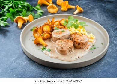 Modern style traditional barbecue pork filet medaillons in cream sauce with chanterelle mushrooms and spaetzle offered as close-up on a Nordic design plate 