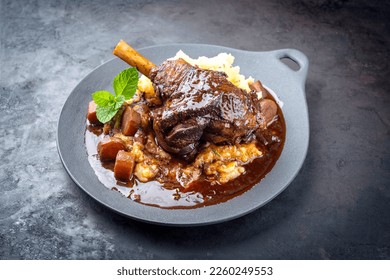 Modern style traditional braised slow cooked lamb shank in red wine sauce with shallots and mashed potatoes offered as top view in a design cast iron plate with copy space 
