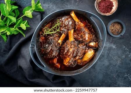 Modern style traditional braised slow cooked lamb shank in red wine sauce with shallots and carrots offered as top view in a design stewpot 