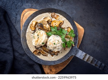 Modern style traditional German cooked porcini mushroom soup with pretzel dumpling and fried potato chips offered as top view in a wrought-iron pan 