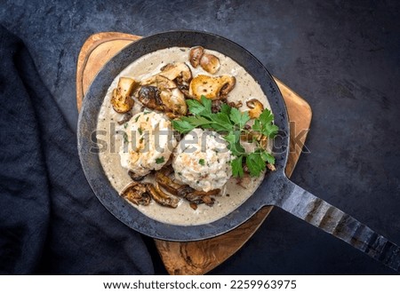 Modern style traditional German cooked porcini mushroom soup with pretzel dumpling and fried potato chips offered as top view in a wrought-iron pan 