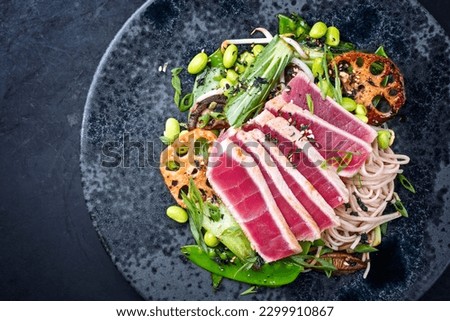 Modern style traditional Japanese gourmet seared tuna fish steak tataki with soba noodles and stir-fried vegetables served as top view on a Nordic design plate with copy space left