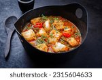 Modern style traditional Spanish seafood zarzuela de pescado with fish served in red sauce as close-up in design pot 