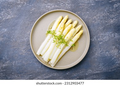 Modern style traditional steamed white asparagus with butter sauce hollandaise and cress served as top view on a Nordic design plate with copy space
