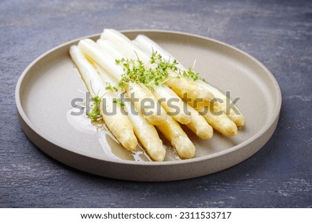 Modern style traditional steamed white asparagus with butter sauce hollandaise and cress served as close-up on a Nordic design plate 