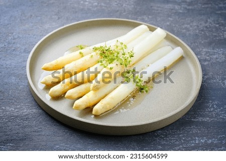 Modern style traditional steamed white asparagus with butter sauce hollandaise and cress served as close-up on a Nordic design plate 