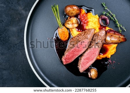 Modern style traditional wild hare back filet braised with wild berries and red wine jus with mashed carrot puree and sweet potato served as top view on Nordic design plate with copy space left