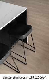 Modern Styled Black Leather Bar Stools With Thin Metal Legs Underneath White Kitchen Counter With Marble Texture On Linoleum Floor With Wooden Print, Vertical Shot