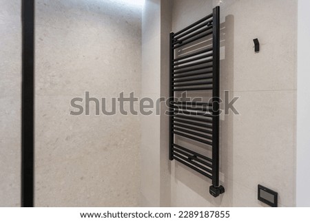 Modern and stylish black heated towel rail with thermostat. Metal heated towel rail on the wall of black marble tiles in the bathroom