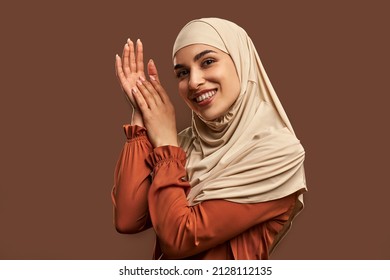 Modern, stylish, fashionable, beautiful Muslim woman dressed in a beige hijab, orange jacket looks at the camera and poses on a brown background. - Powered by Shutterstock