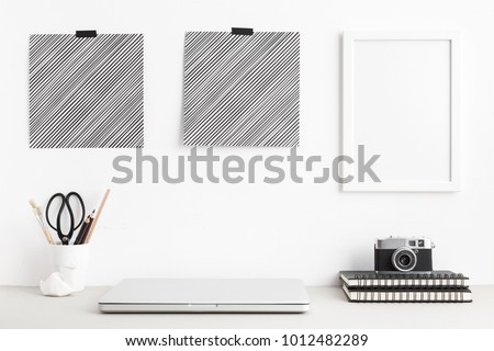 Modern and stylish workspace with laptop computer closed, empty phoro frames, posters office supplies, camera at home or studio. Mock up.