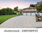 Modern suburban home with a large driveway and well-maintained lawn at sunset