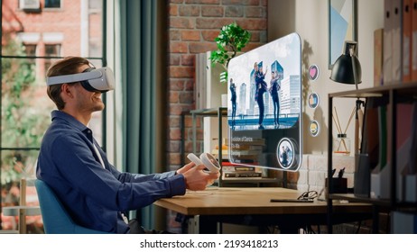 Modern Successful Man Sitting In Living Room At Home, Using Virtual Reality Headset With Controllers To Check Social Media Application. Young Male Watching A Dance Music Video Clip.