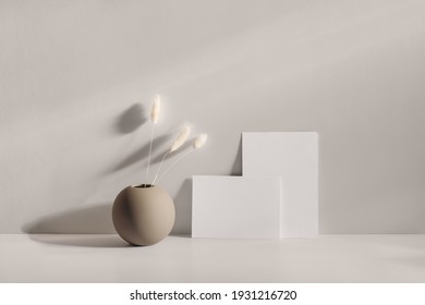 Modern summer stationery still life scene. Beige round vase with dry lagurus grass. Table background in sunlight. Blank business card, invitation mockups lean on champagne wall, long shadows. 