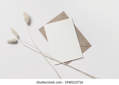 現代の夏用文房具は、まだ生きている。 オバタスの葉と船のエンベロープ。 白いテーブル背景に白いグリーティングカード、バニーテールグラスのモックアップシーン。 平面、上面図。の写真素材