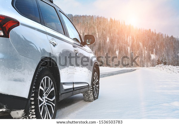 Modern Suv four wheel drive car stay on roadside of
winter road. Family trip to ski resort concept. Winter or spring
holidays adventure. car on winter snowy road in mountains in sunny
day.